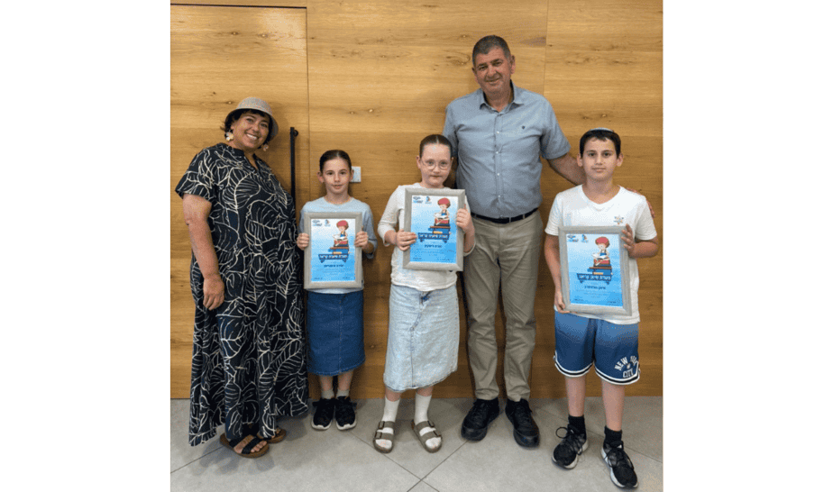חמשה אנשים עומדים מול קיר עץ, שני מבוגרים ושלושה ילדים, מחזיקים תעודות או פרסים, באירוע חינוכי או קהילתי.